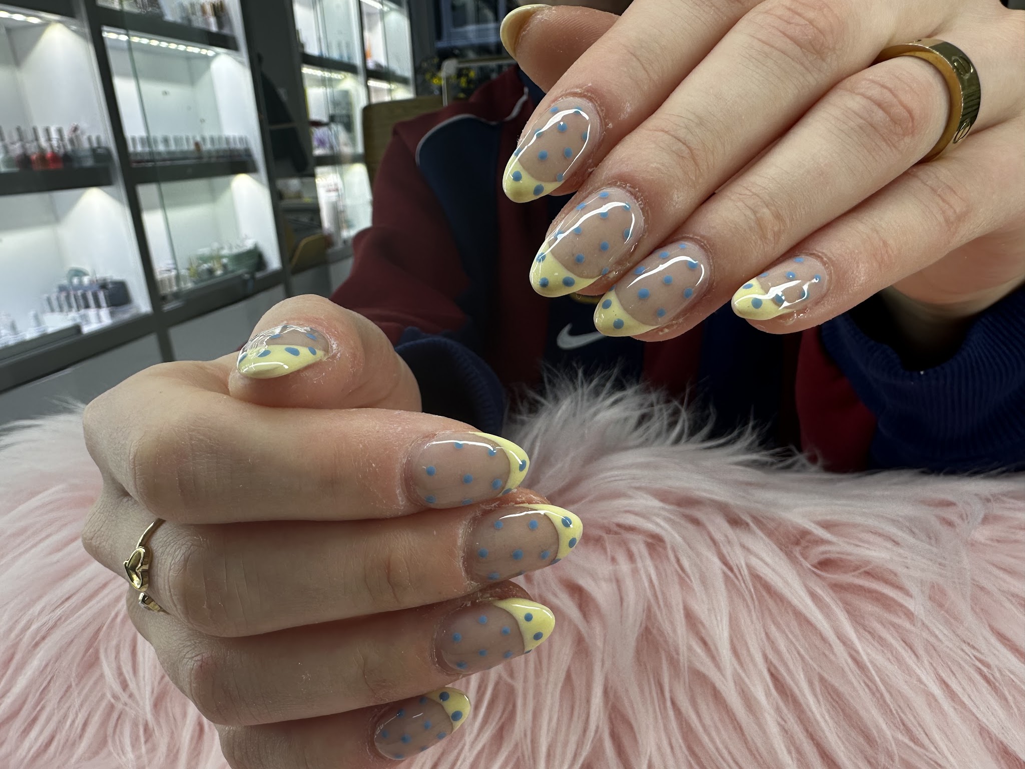 Amandelnagels met zachtgele French en stipjes, met de kleurenwand op de achtergrond