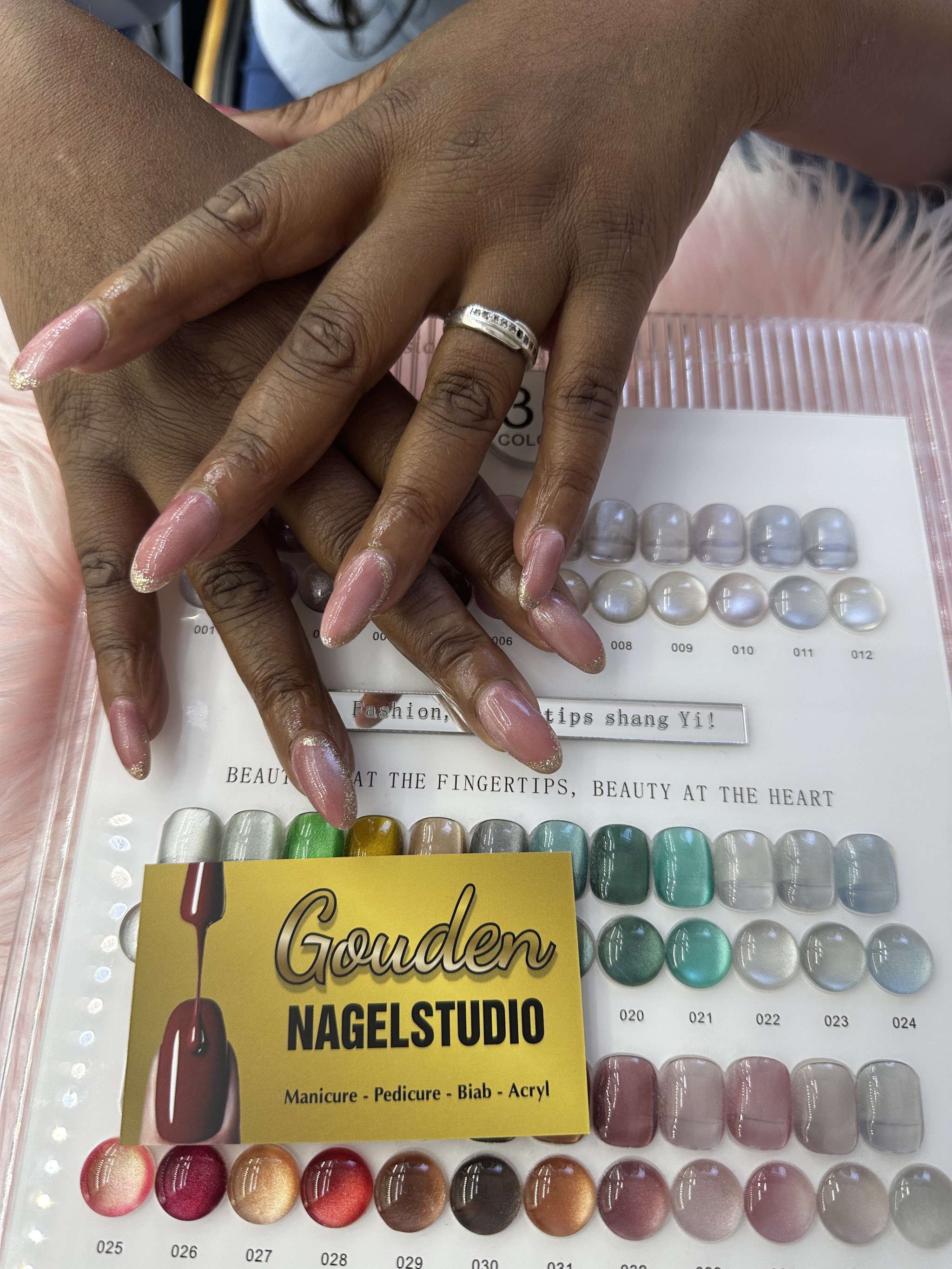 Nude amandelnagels met glitterpunten boven de kleurenkaart met gellak, met het gouden visitekaartje